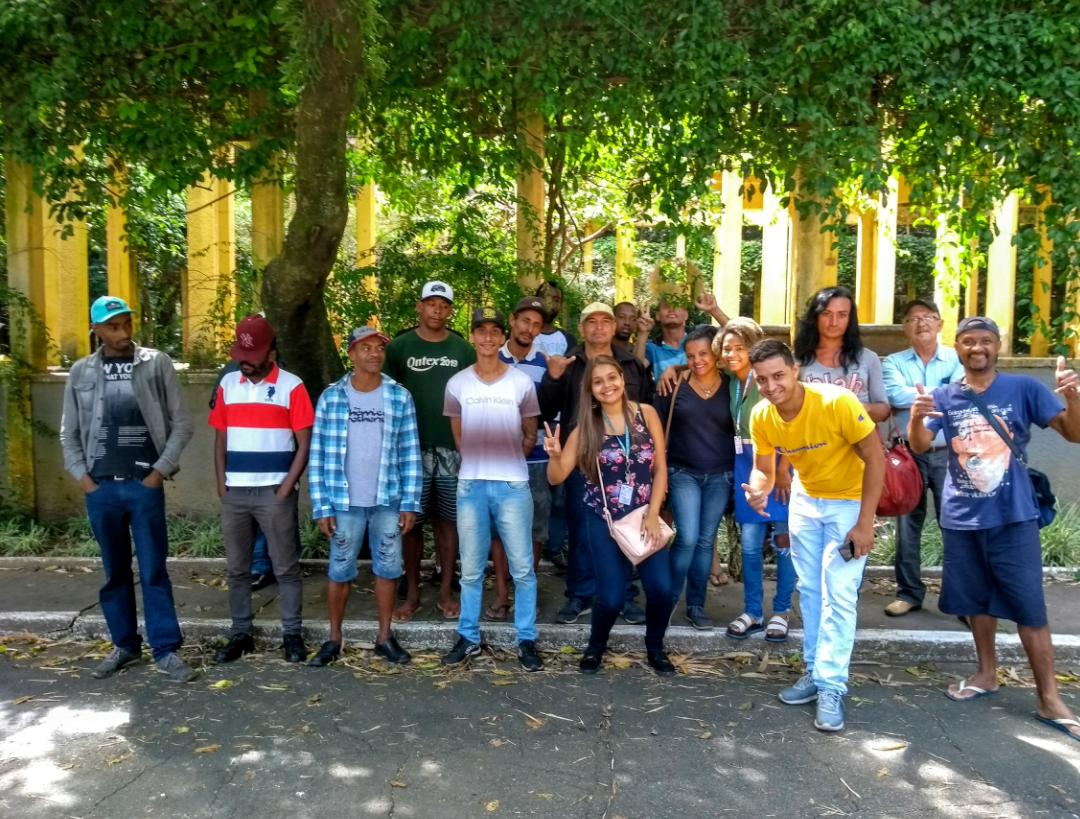 : Dezenas de homens e mulheres estão na parte de dentro de um parque. Todos olham e fazem pose para a foto.