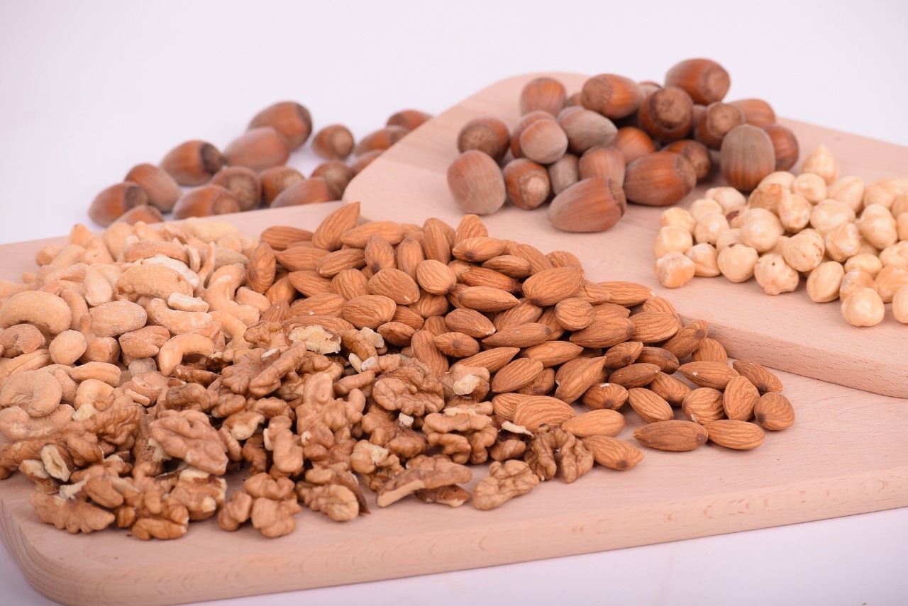 Em uma bandeja de madeira há diversos tipos de sementes oleaginosas como nozes, castanhas e amêndoas.