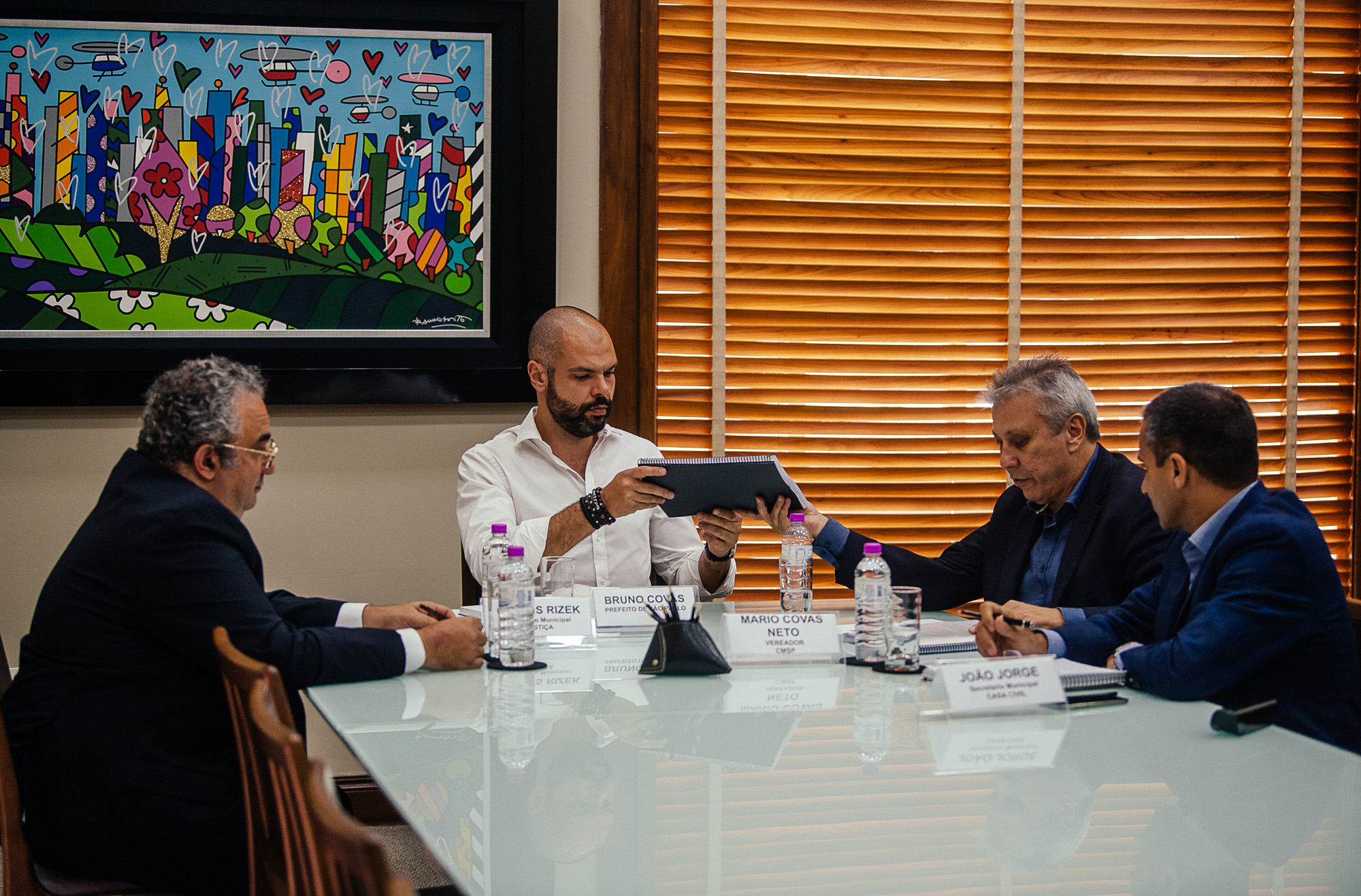 sala de reunião com a presença do Prefeito, do Secretário de Justiça, Rubens Rizek, do Secretário da Casa Civil, João Jorge e do vereador Mario Covas Neto.