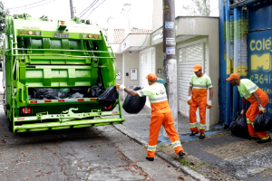 Coletores avançam em direção ao caminhão do lixo em rua da cidade