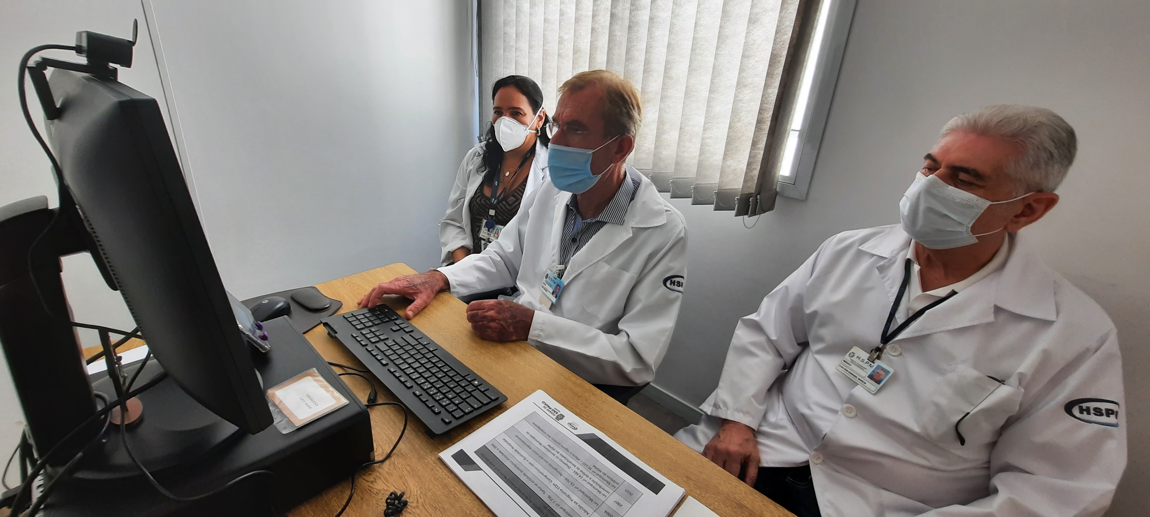 Foto com três profissionais do hospital, dois homens e uma mulher, em frente ao computador