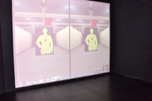 #PraTodosVerem-  A Imagem mostra duas silhuetas humanóides no estande de tiro em tela virtual.