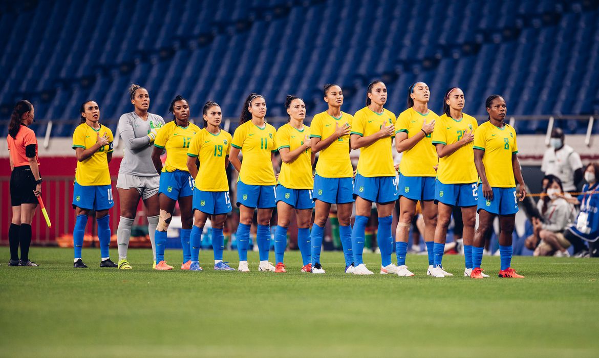 Jogadoras da seleção feminina ouvindo o hino nacional em partida oficial.