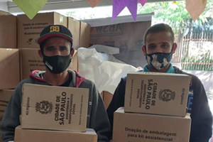 #PraCegoVer Três pessoas com máscaras de proteção contra a Covid em colaboração descarregam cestas básicas de um caminhão
