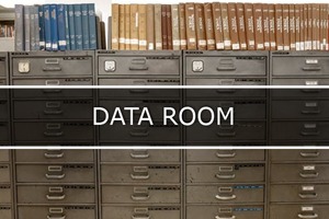 Fotografia que mostra armário cheios de gavetas para guarda documentos e em cima tem vários pasta  na vertical e no meio escrito Data Room