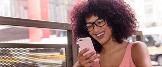 #PraTodosVerem Foto de uma mulher de óculos interagindo com um celular. O detalhe é a cor rosa do aparelho que combina com a blusa