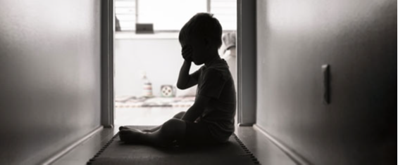 #PraTodosVerem: uma criança é fotografada no final de um corredor de uma moradia. A foto mostra sua figura desfocada. Ela está sentada e com a mão no rosto como se estivesse chorando