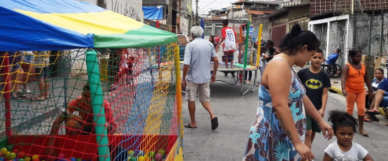 Diversas pessoas andando em uma Rua de Lazer. É possível ver atividades como piscina de bolinha e cama elástica.