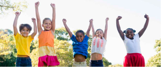 PraTodosVerem: Cinco crianças na faixa de cinco a sete anos ilustram essa foto. Elas estão pulando com os braços levantados, meninos e meninas brancos e pretas.