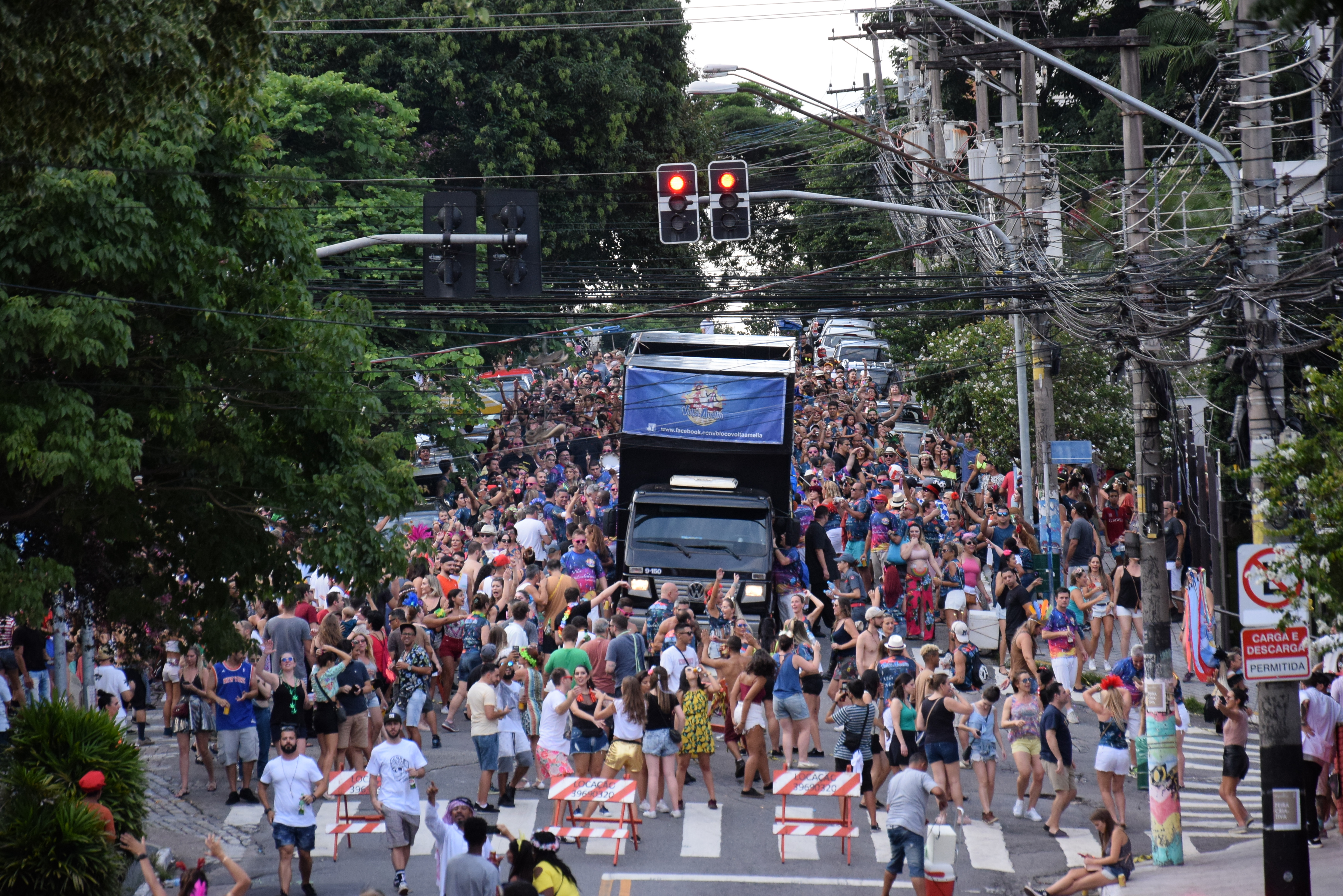 A imagem mostra uma imagem de um trio elétrico desfilando na rua e uma multidão de pessoas ao redor.