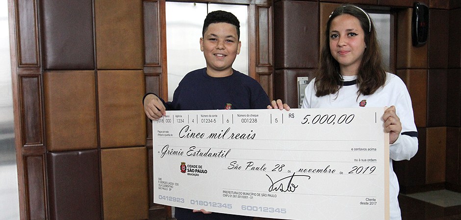 Foto de dois estudantes recebendo o cheque simbólico do grêmio estudantil.