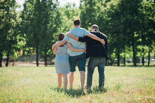 Foto de três pessoas, um homem, uma mulher e uma criança, abraçadas e de costas em um parque