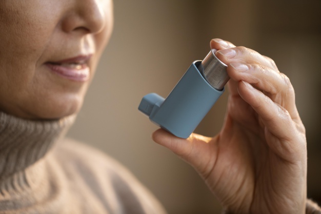 Foto do rosto de uma mulher, com foco na boca, segurando uma bombinha azul para asma