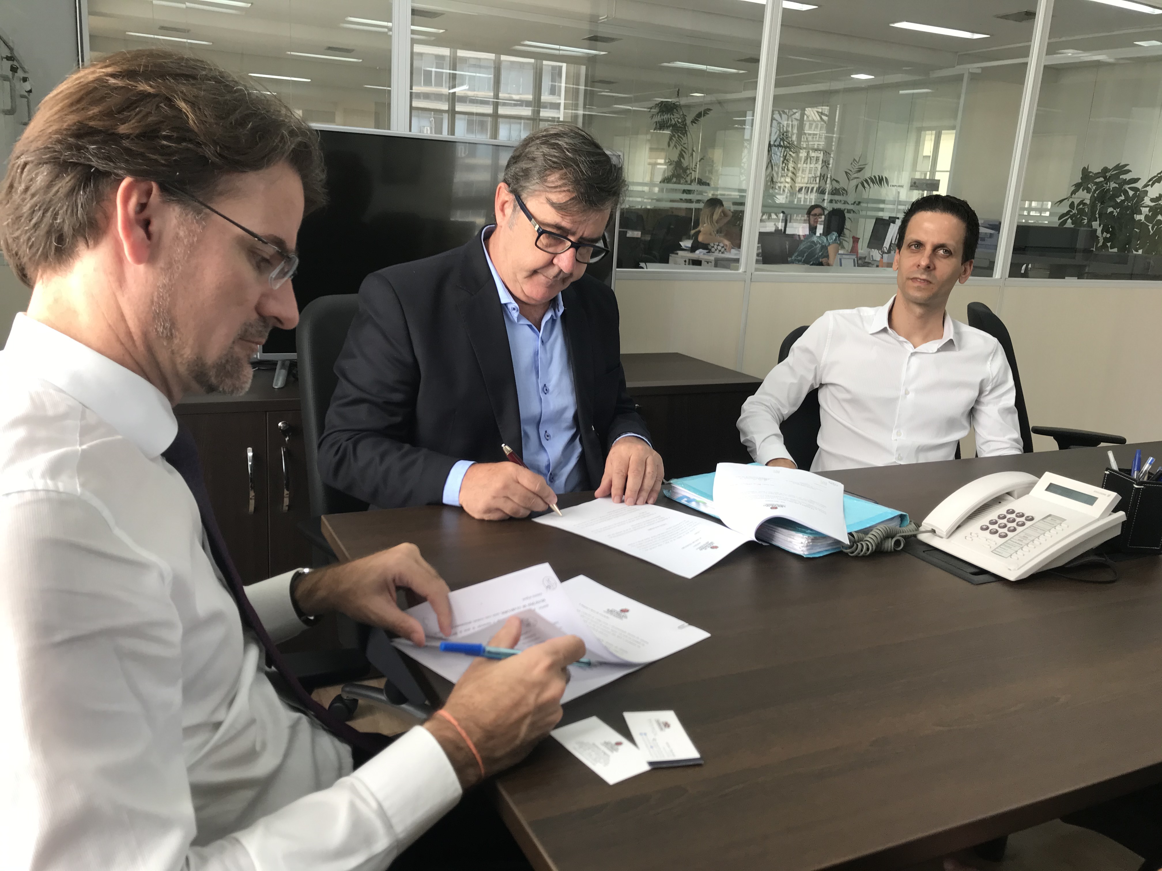 imagem com o controlador Gustavo Ungaro, o Secretário de Justiça de Guarulhos, Airton Trevisan e Rodrigo Morello. eles assinam um documento