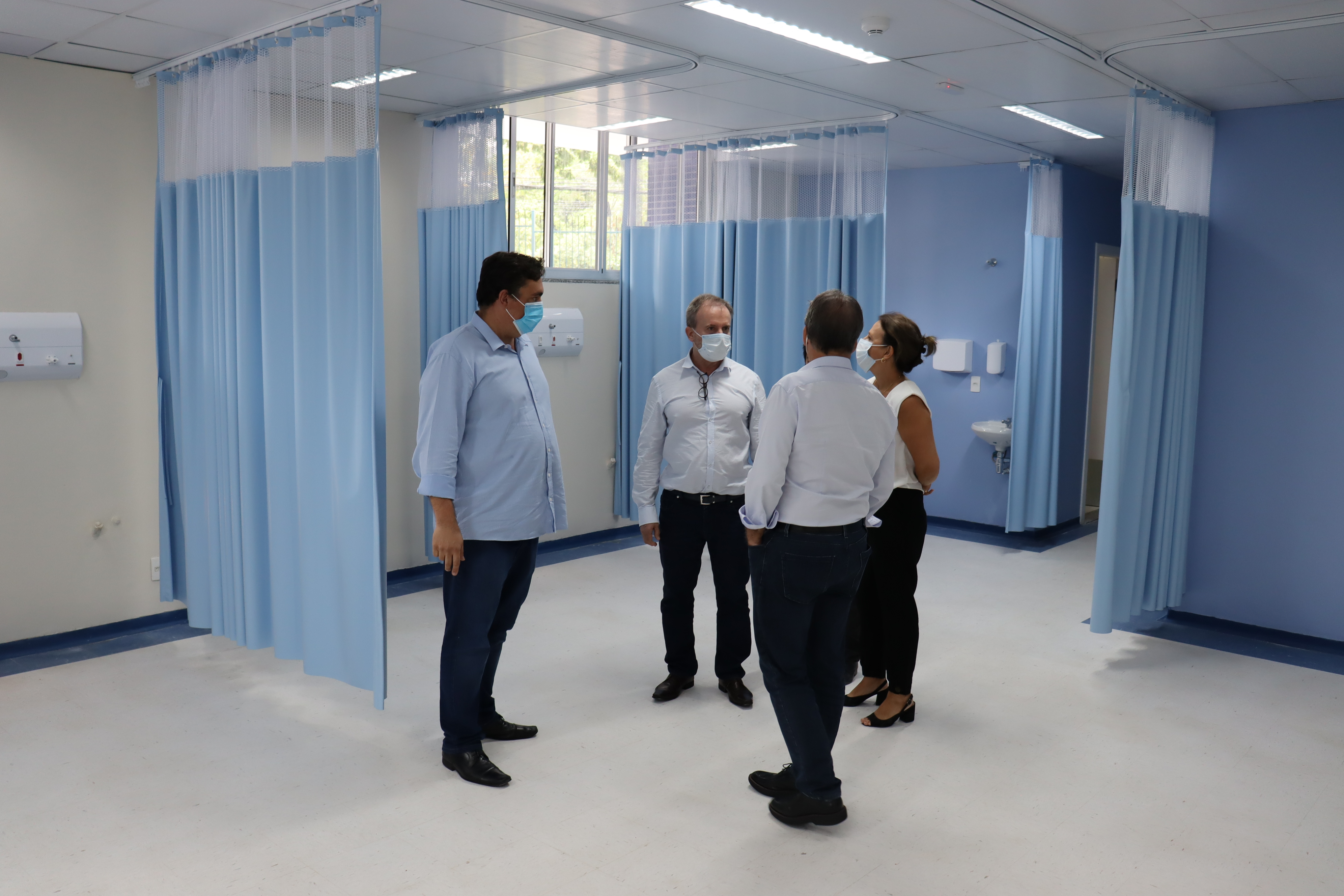 Foto mostra três homens e uma mulher no local onde será a enfermaria do PS. As cortinas azuis já foram instaladas.