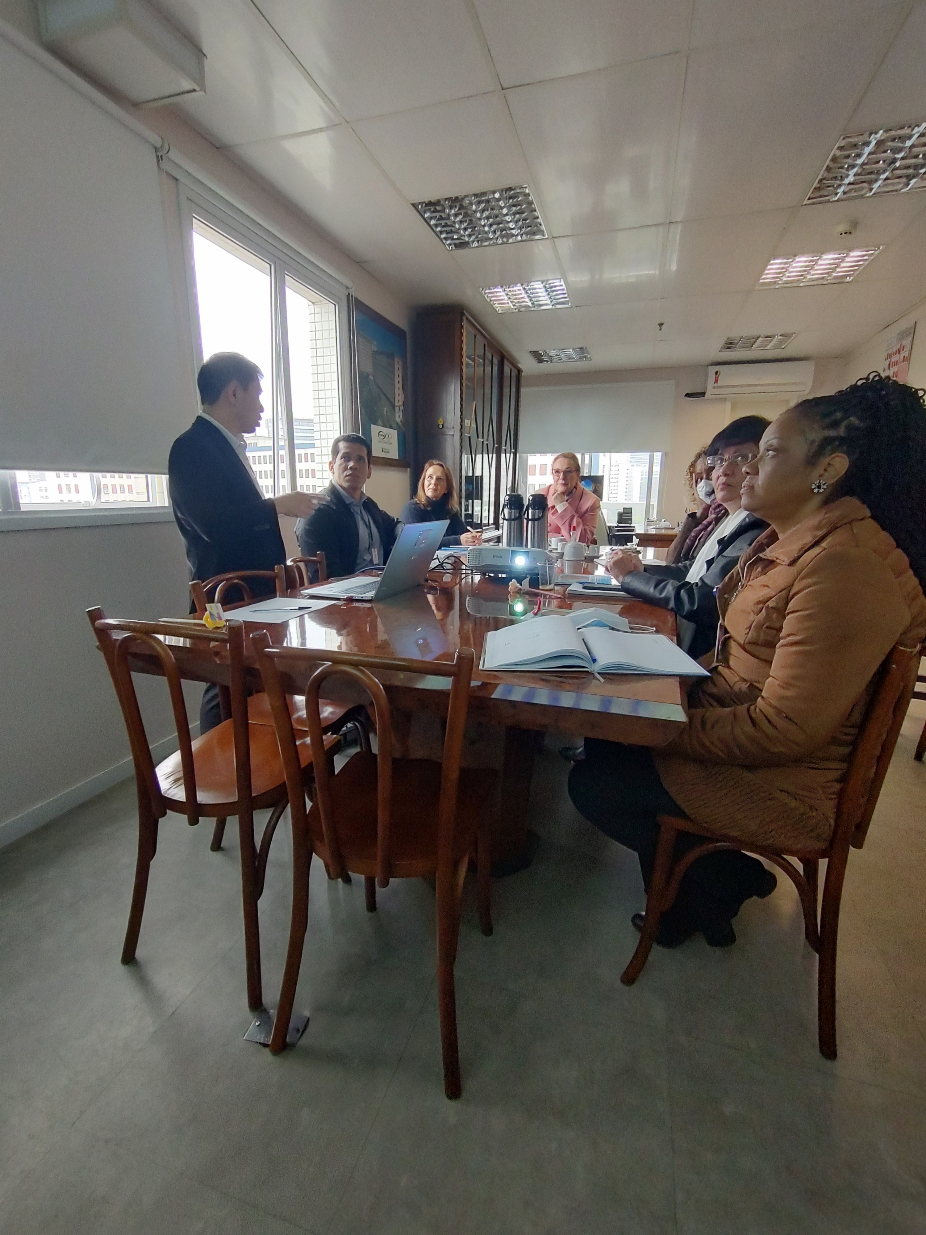 Imagem dos participantes sentados à mesa de reuniões