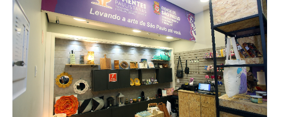 Na foto mostra a nova fachada da loja do programa Mãos e Mentes Paulistanas, a fachada esta na cor roxa, também é possivel ver alguns itens artesanais vendidos na loja