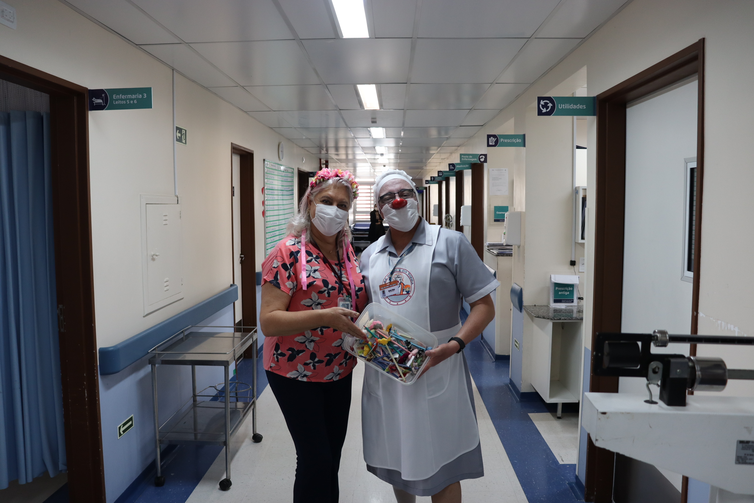 Fotografia da Coordenadora do CAV e do voluntário fantasiado de enfermeira, com a cesta de brindes nas mãos