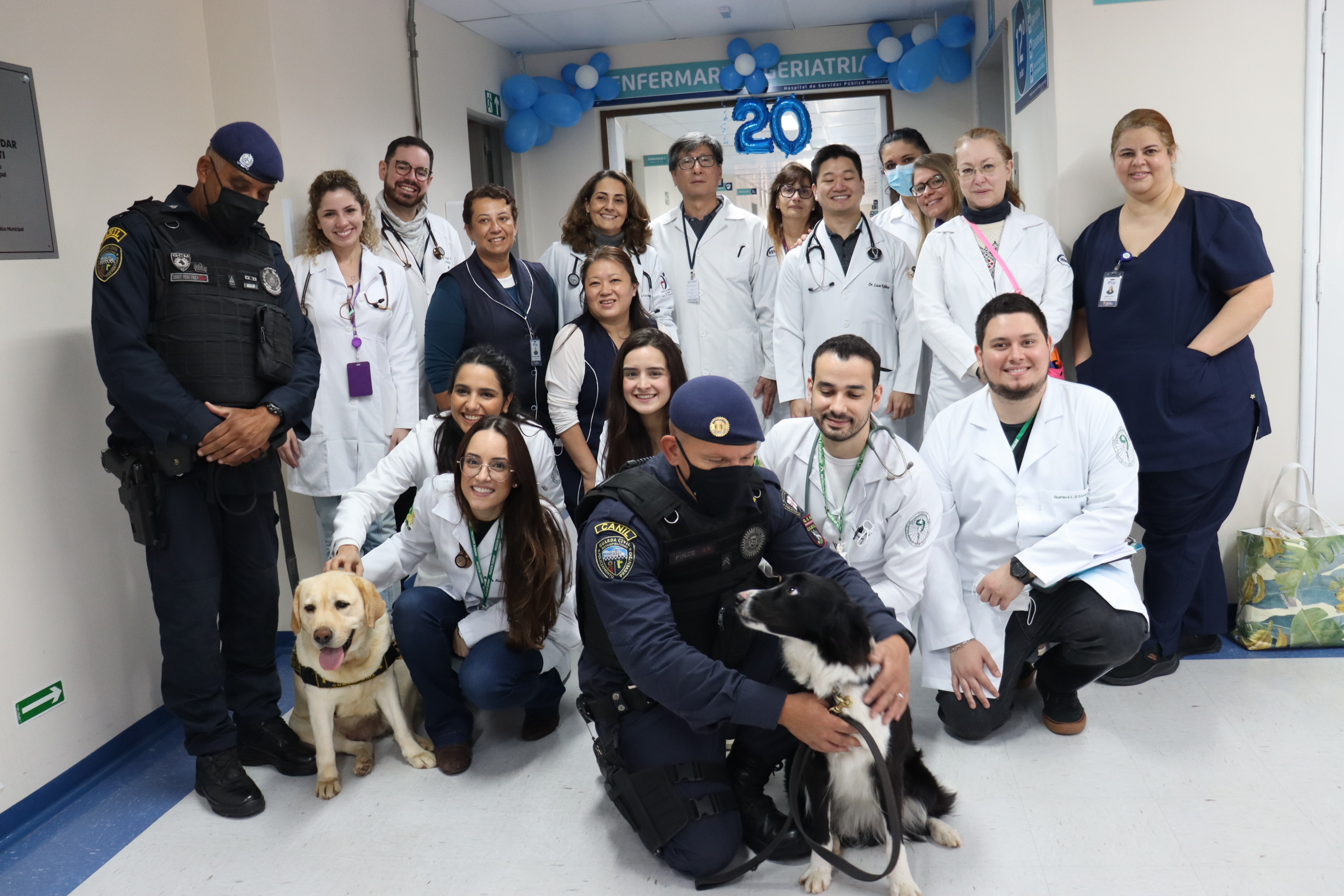 Fotografia do grupo de profissionais da equipe de Geriatria, com os guardas e com os cães da Guarda Civil Metropolitana (GCM).
