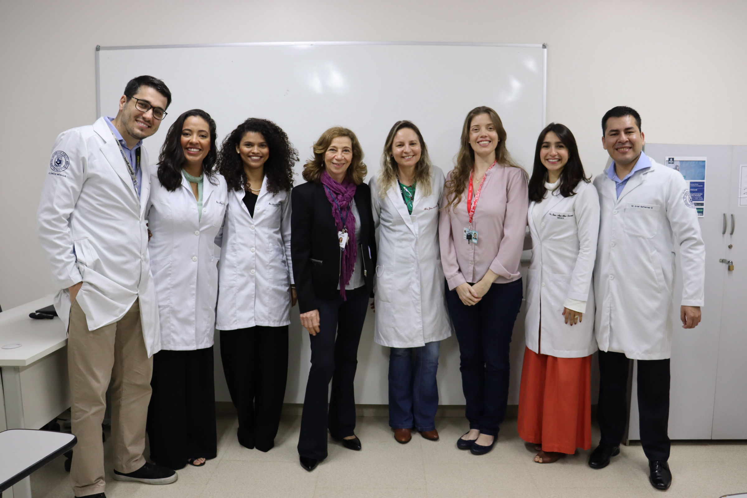 Foto de 8 médicos residentes em pé na sala de aula