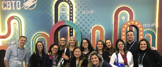Na imagem, está pessoas reunidas para foto. Ao fundo, em um painel, está a palavra CBTD em vários lugares do painel.