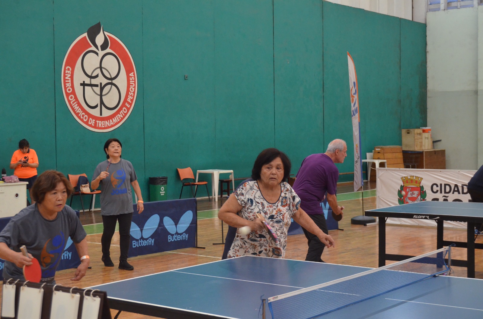 Na imagem, participantes jogando tênis de mesa no Jogos Municipais da Pessoa Idosa 2023.