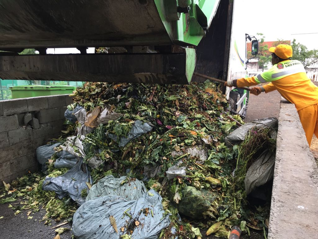 caminhão de coleta de lixo descarregando resíduos de feiras no pátio de compostagem