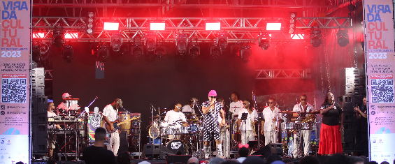 Panorâmica do Palco Para Inglesa, lotado, com show de Carlinhos Brown e banda. Intérprete de Libras ao lado direito, público acompanha.