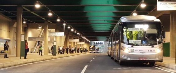 Terminal de ônibus com pessoas e ônibus para a direita da foto
