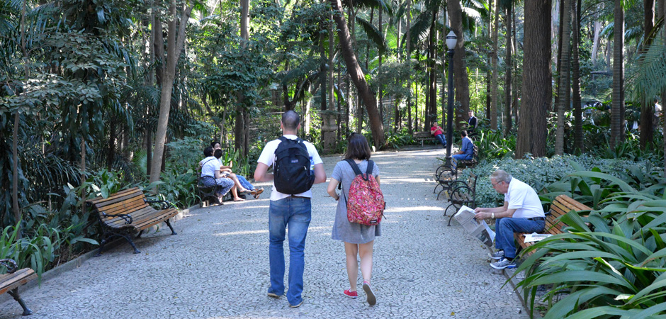 Foto de uma trilha do Parque Trianon com alguns bancos do lado direito e esquerdo e pessoas caminhando ou sentadas lendo.