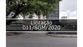 Fotografia mostra  o terreno  vazio e no fundo da foto tem prédios, no canto na esquerda tem arvore e no meio escrito Licitação 011/SGM/2020