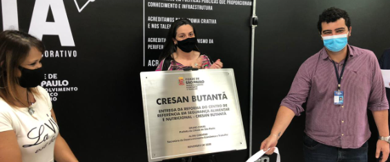 a imagem mostra a secretária aline cardoso acompanhada de 2 pessoas enquanto apresenta a placa de inauguração do cresan butantã