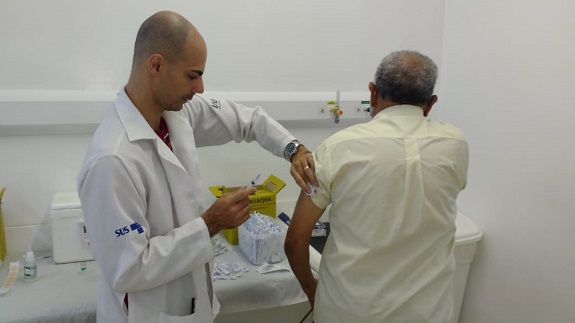 #pracegover na imagem um médico aplica a vacina num munícipe, que está de costas para a câmera.