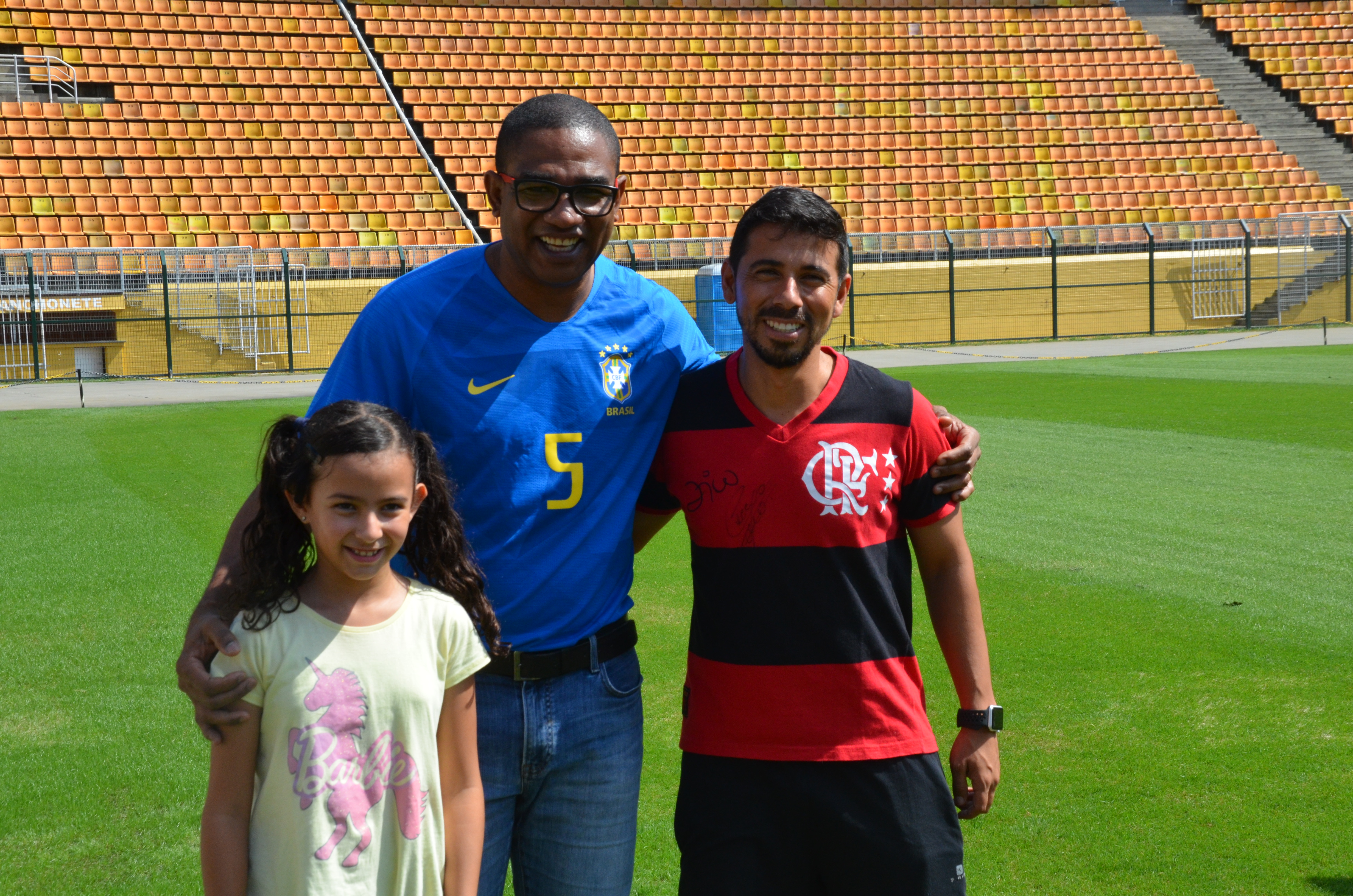 César Sampaio posa para foto no gramado do Pacaembu ao lado de homem com camisa do Flamengo e uma criança.