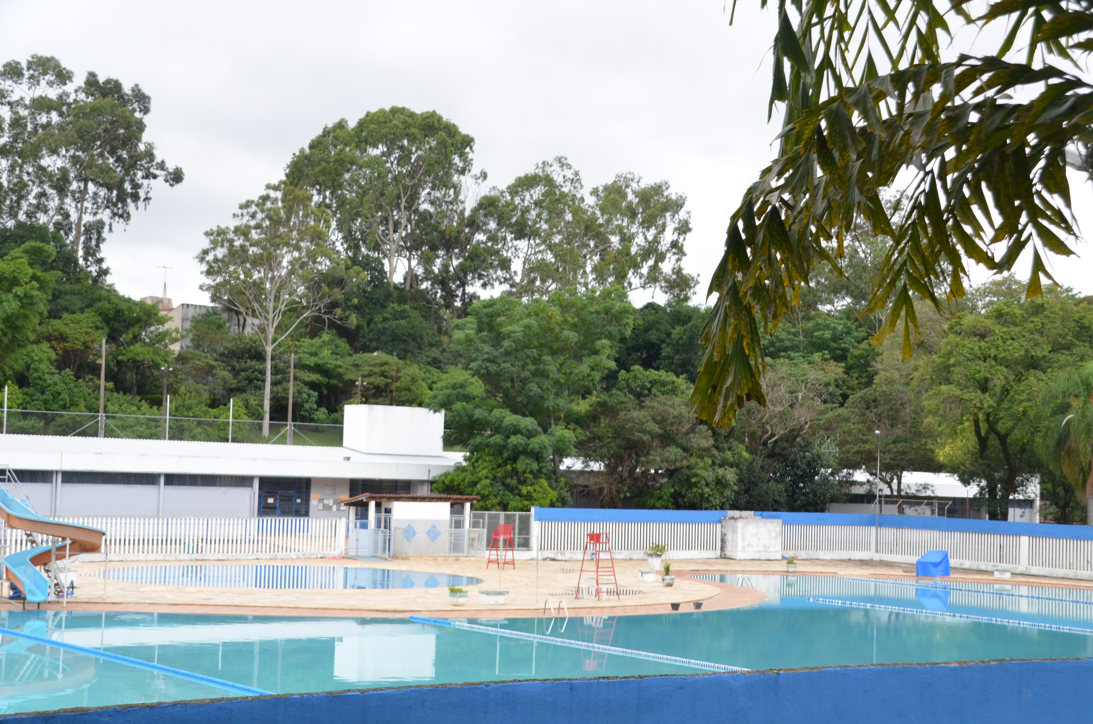 Centro Esportivo Pelezão, na imagem piscinas, bancos de salva-vidas e muitas árvores em um dia nublado.