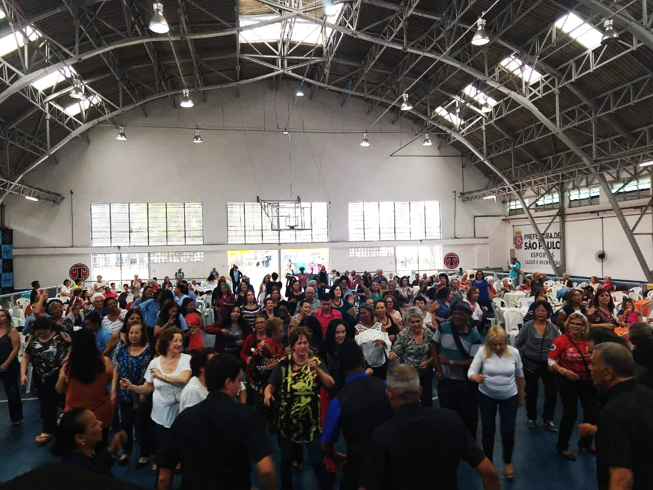 Diversas pessoas, grande maioria de 3ª idade, lotam o ginásio do Centro Esportivo Tietê, no Baile da Virada.