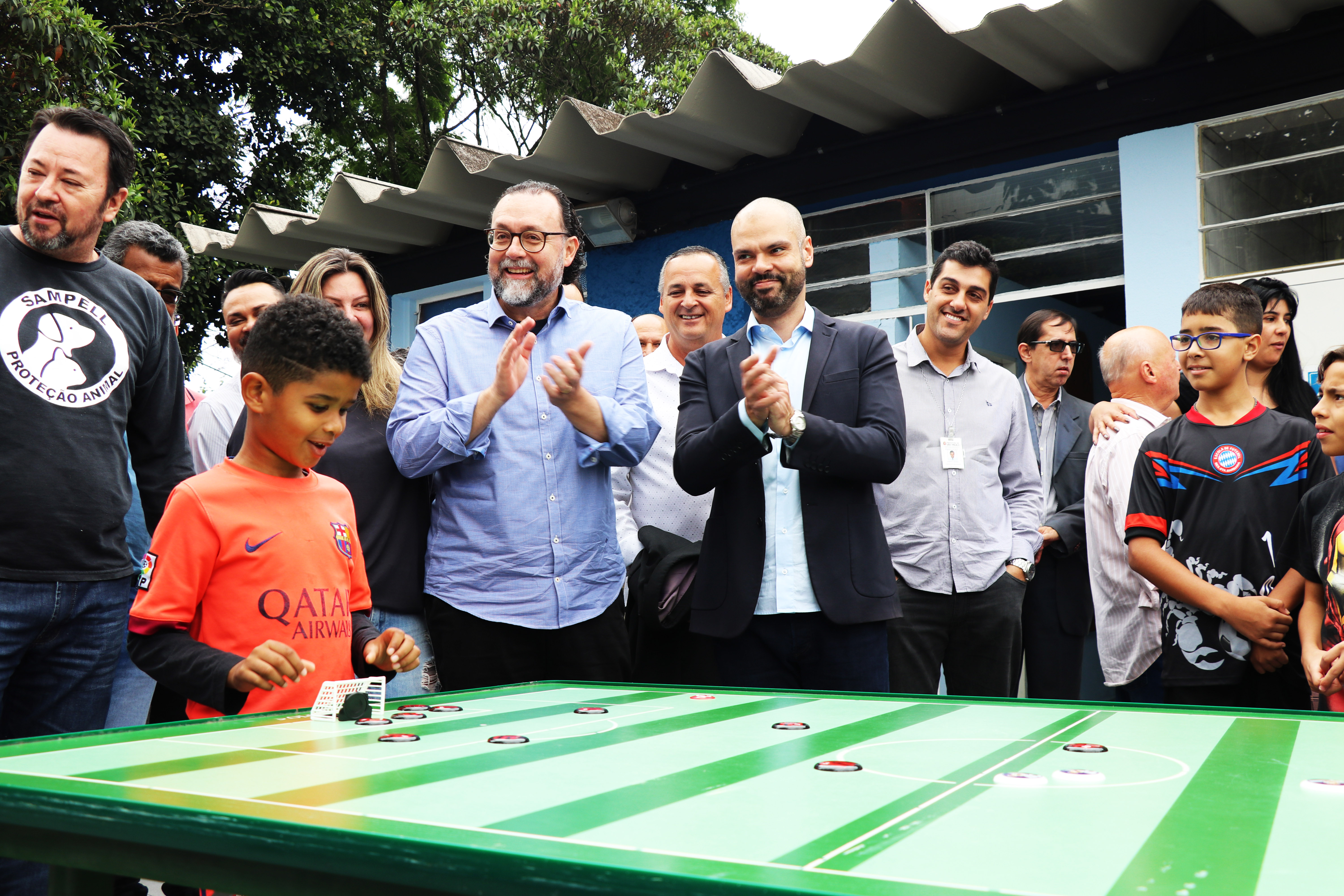 Secretário Municipal de Esportes e Lazer, Carlos Bezerra Jr., e prefeito Bruno Covas aplaudem jogada de uma criança no futebol de botão.