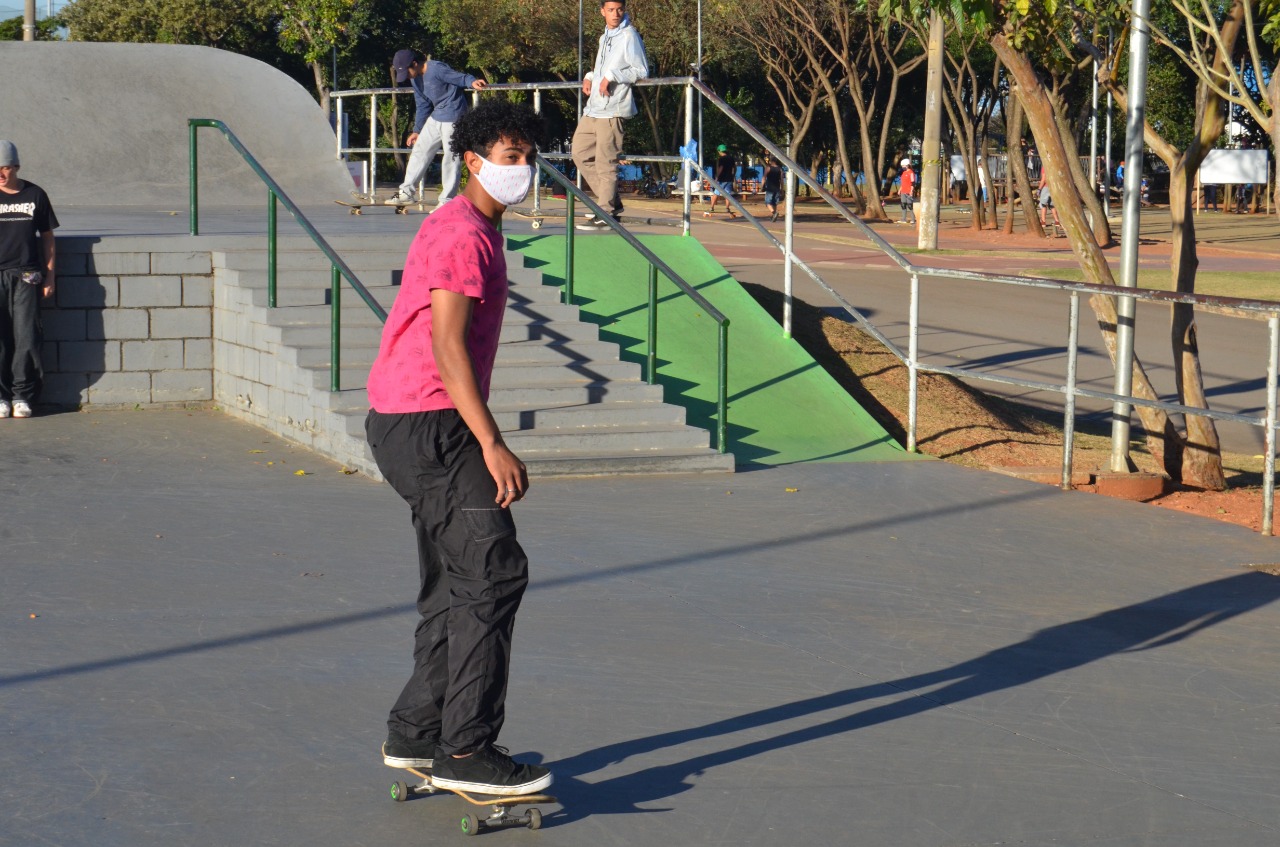 Na imagem, atleta de skate de máscara na pista do Centro de Esportes Radicais em um dia ensolarado.