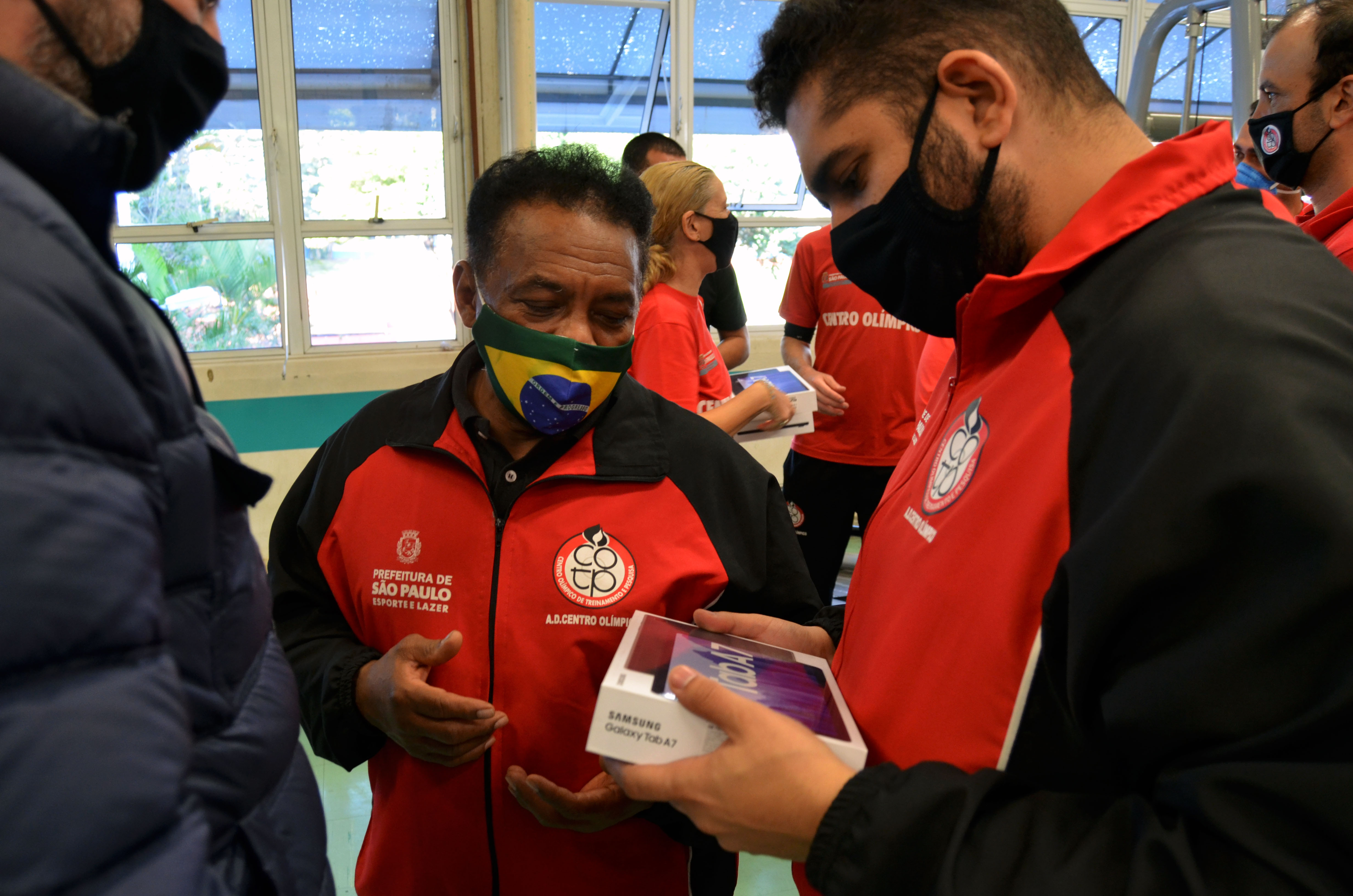 Professor Messias Gomes, do boxe, mostra a caixa do tablet ao secretário municipal de Esportes e Lazer, Thiago Milhim. Ambos estão de máscaras.