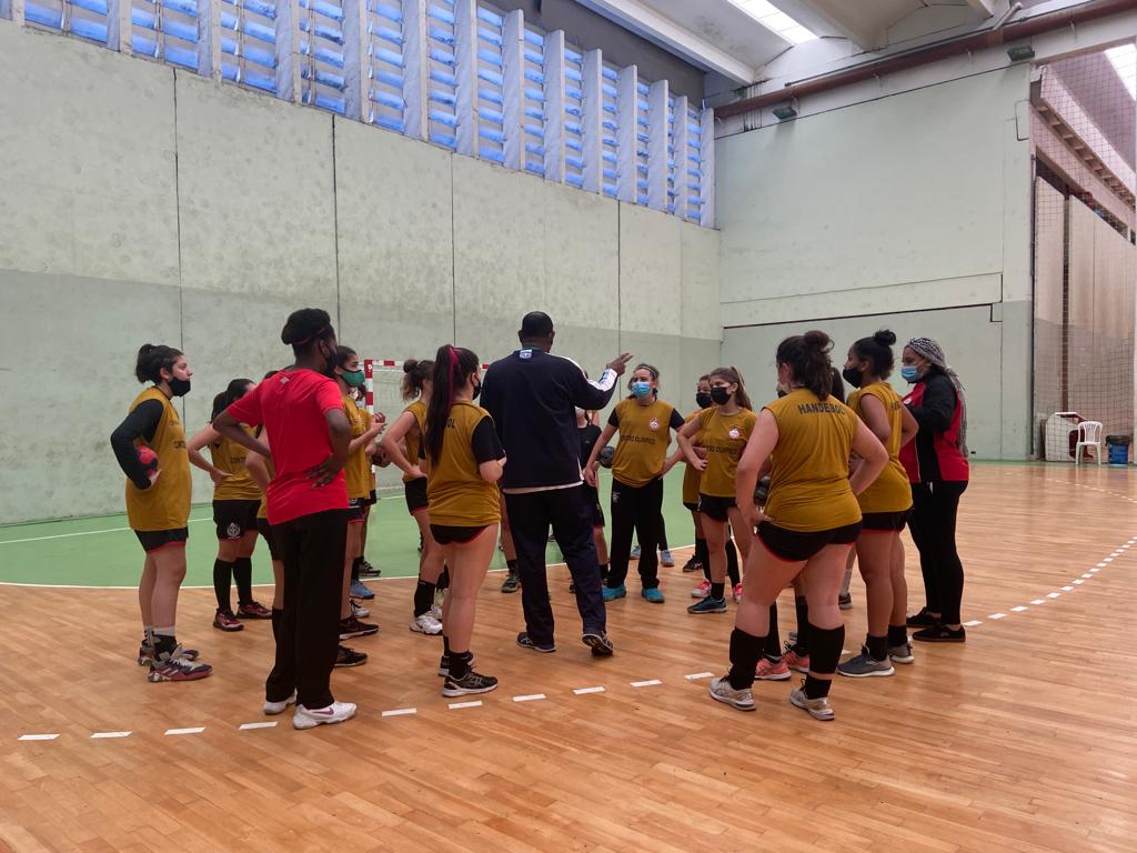 Ateltas e comissão técnica de handebol do Centro Olímpico reunidos de costas para a foto atentos às instruções do treinador.