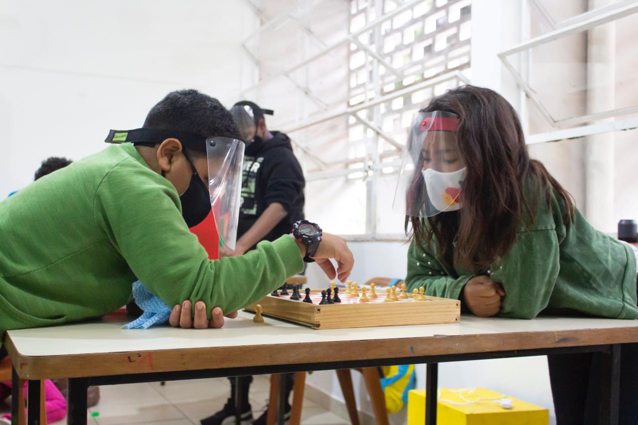 Duas crianças, com todo o protocolo sanitário, jogam xadrez durante a oficina de educação financeira.