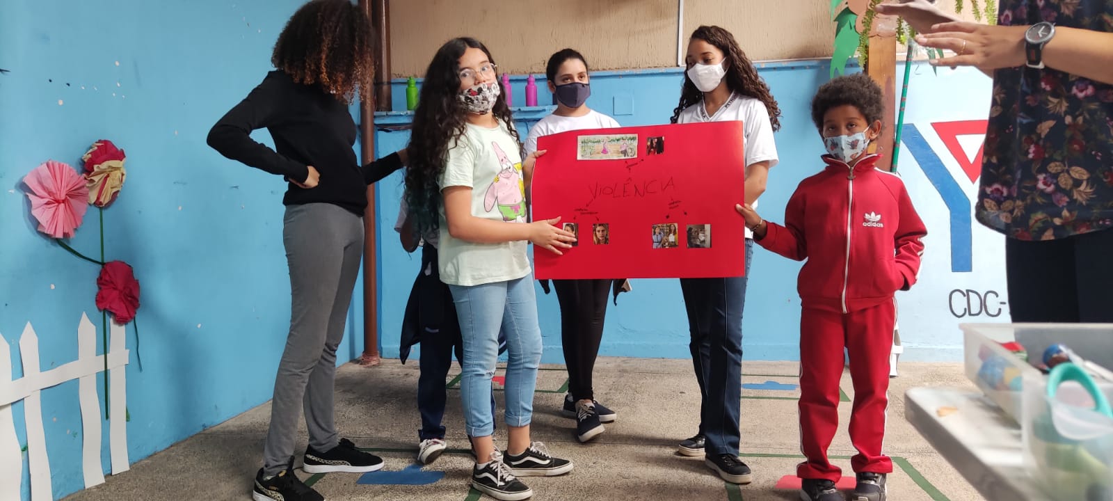 5 Crianças segurando um cartaz com imagens de violência, ao fundo o símbolo da ACM, e a frente homem mexendo no celular.