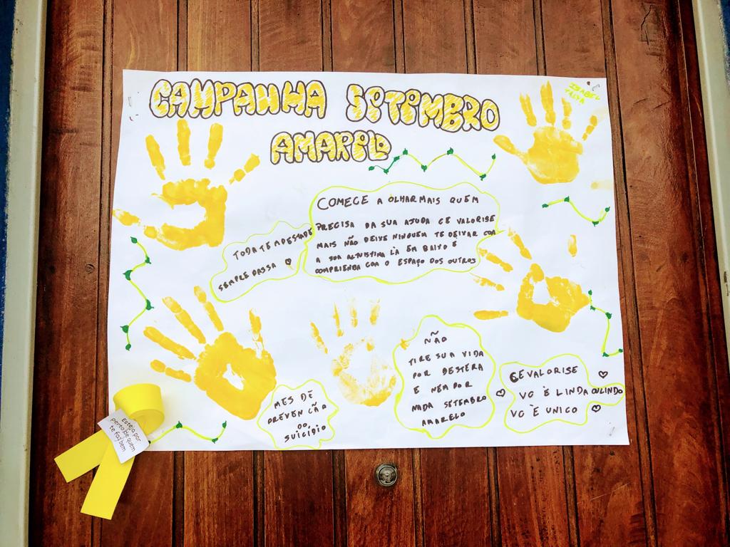 Um cartaz feito pelas crianças sobre o “Setembro Amarelo”, pintado com canetinhas amarelas e marcas de mão das crianças de tinta amarela.
