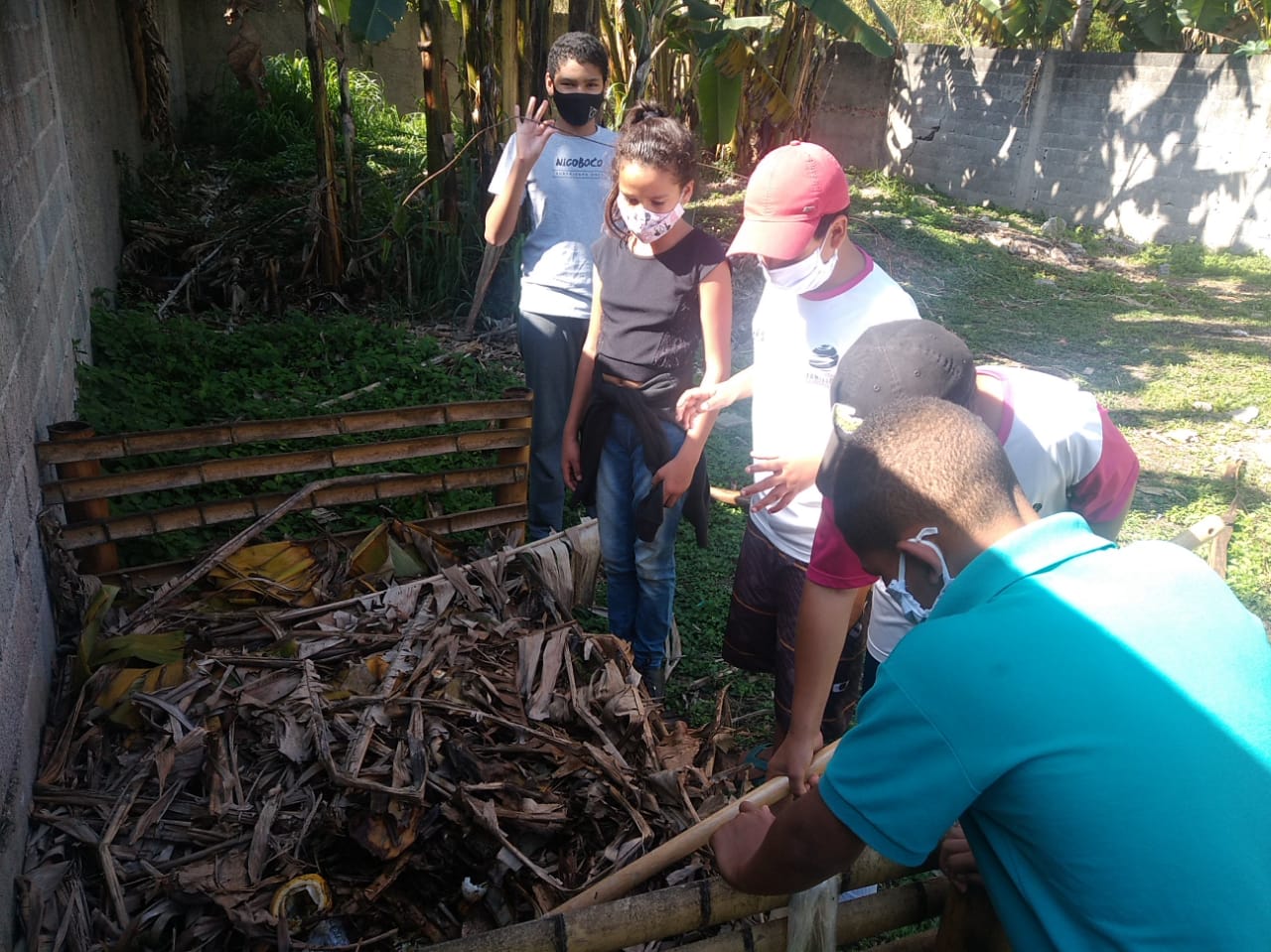 Cinco crianças em volta do sistema de compostagem participam dos cuidados diários do local.