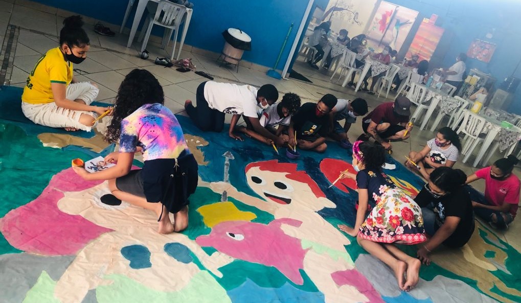 Diversas crianças reunidas e trabalhando na pintura do mural durante a atividade.