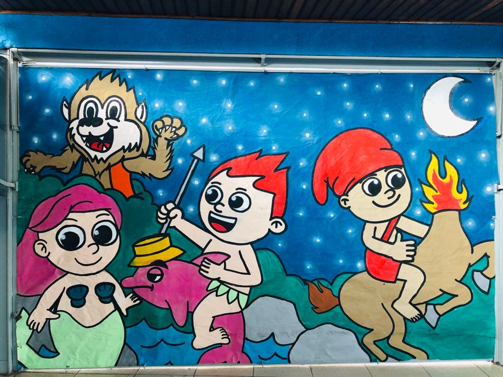 Mural pintado pelas crianças durante a atividade, com desenhos dos personagens do folclore: Saci-pererê, Lobisomem, Boto-cor-de-rosa, Iara e o Curupira