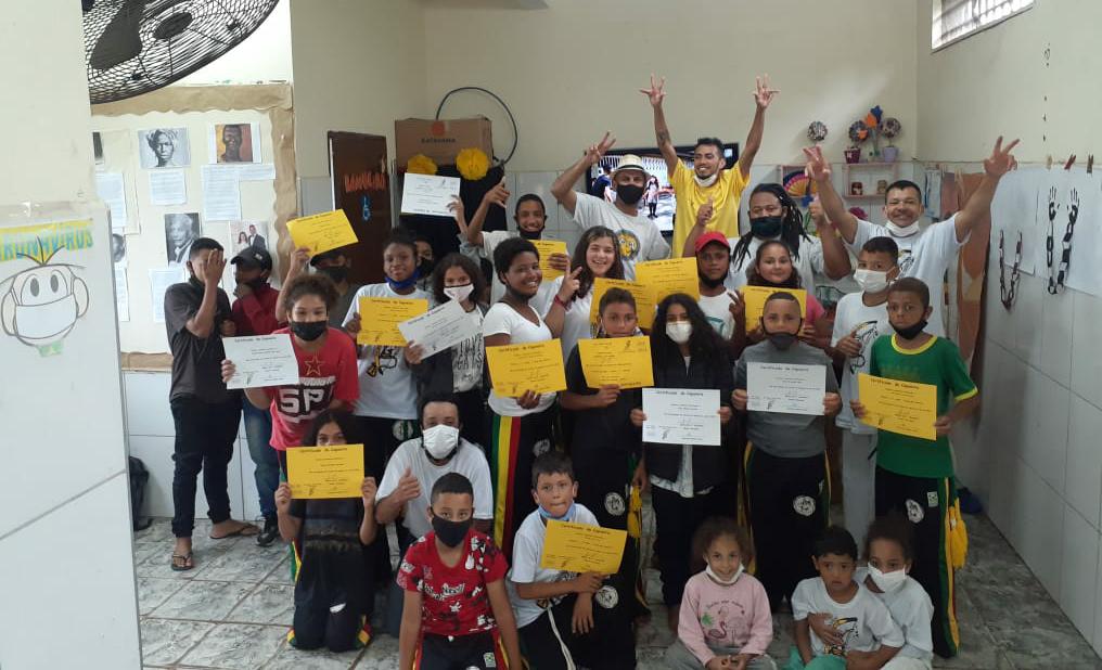 : A turma da oficina de capoeira se junta para tirar uma foto com seus certificados em suas mãos. 