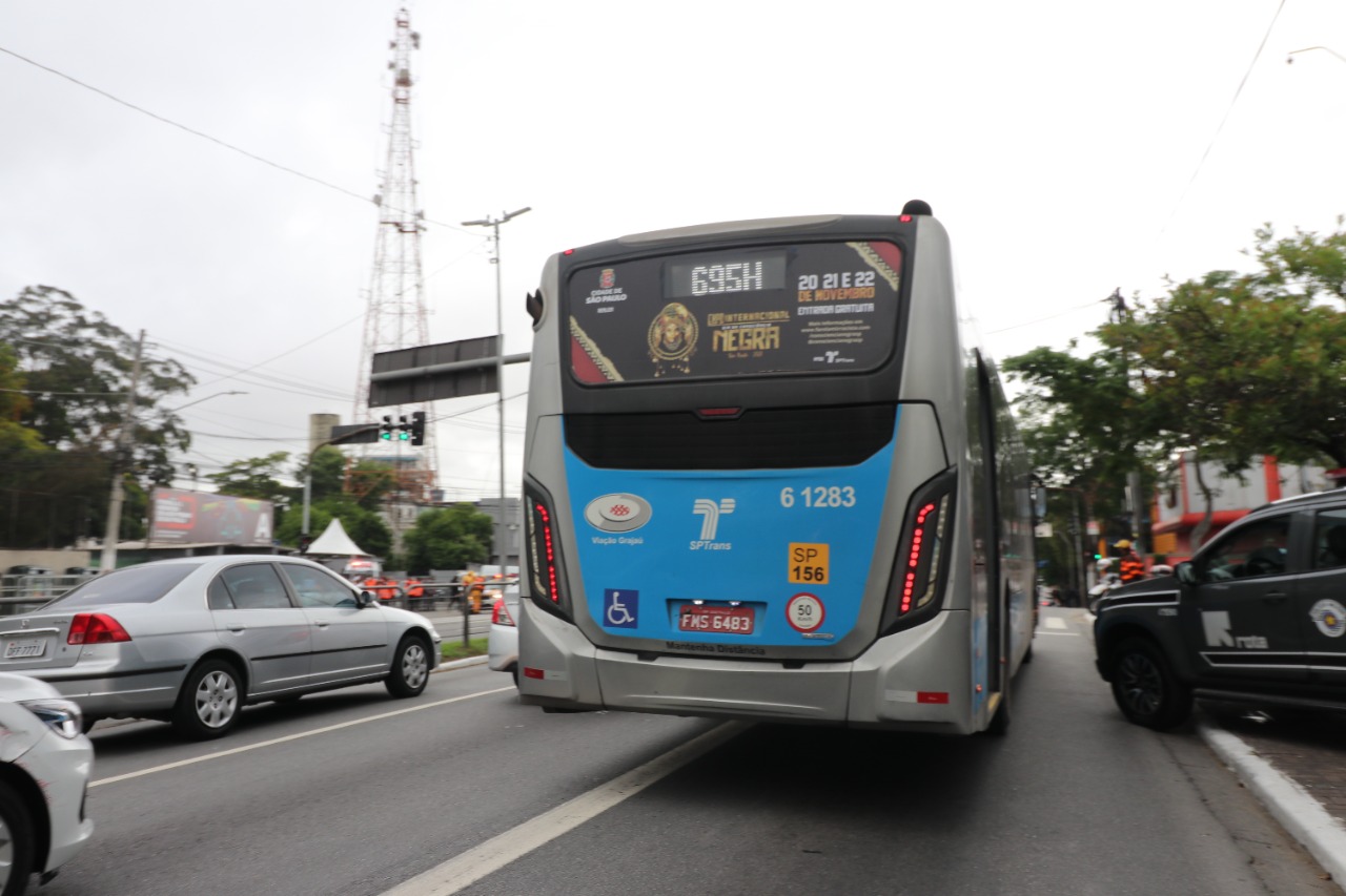Imagem de um ônibus SPTrans em movimento em uma avenida, com adesivo da Expo Internacional da Consciência Negra no vidro do Fundo deste ônibus