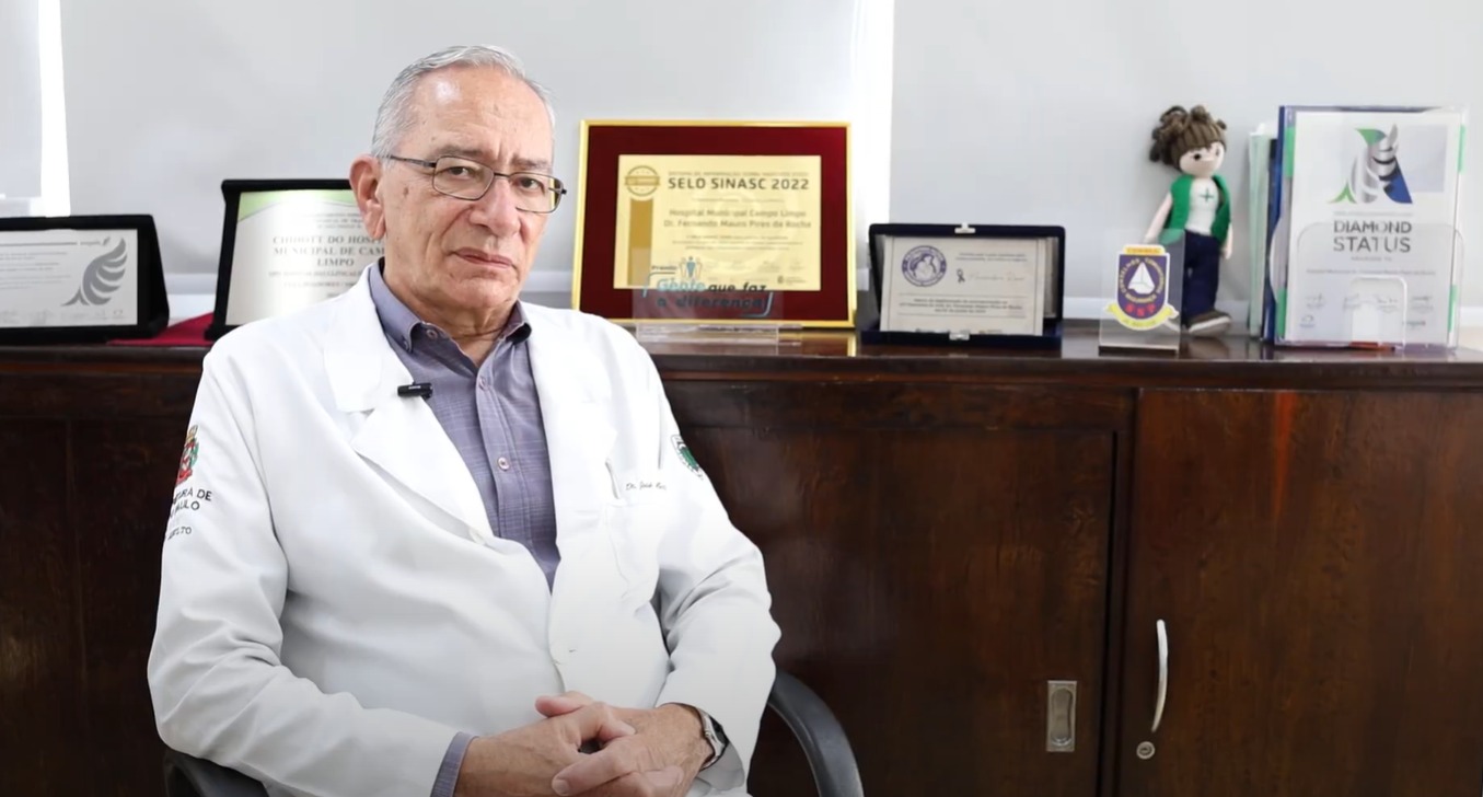 A foto mostra Nassif, um homem branco de cabelos grisalhos, vestindo um jaleco branco, sentado em um escritório.