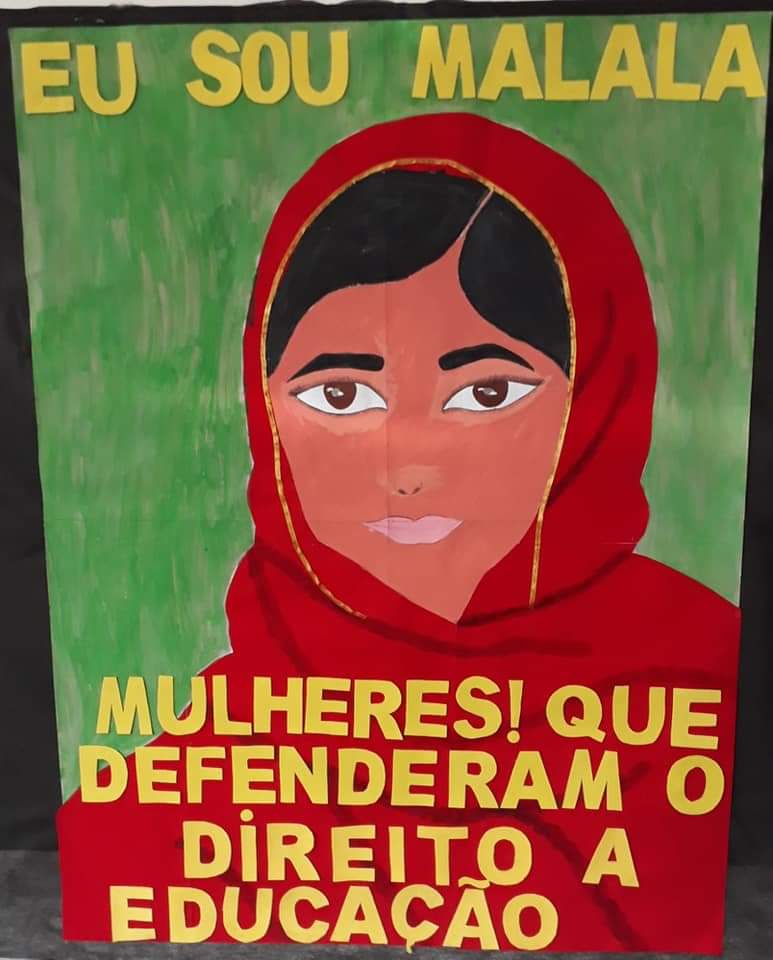 Um painel verde com nderam o direuma moça usando uma roupa com burca vermelha com frase “Eu Sou Malala. Mulheres que defeito da educação” em amarelo